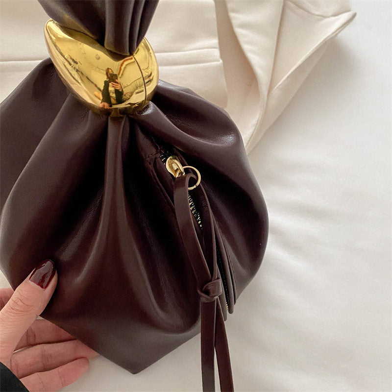 Brown leather drawstring bag with gold clasp held by a hand on a light background