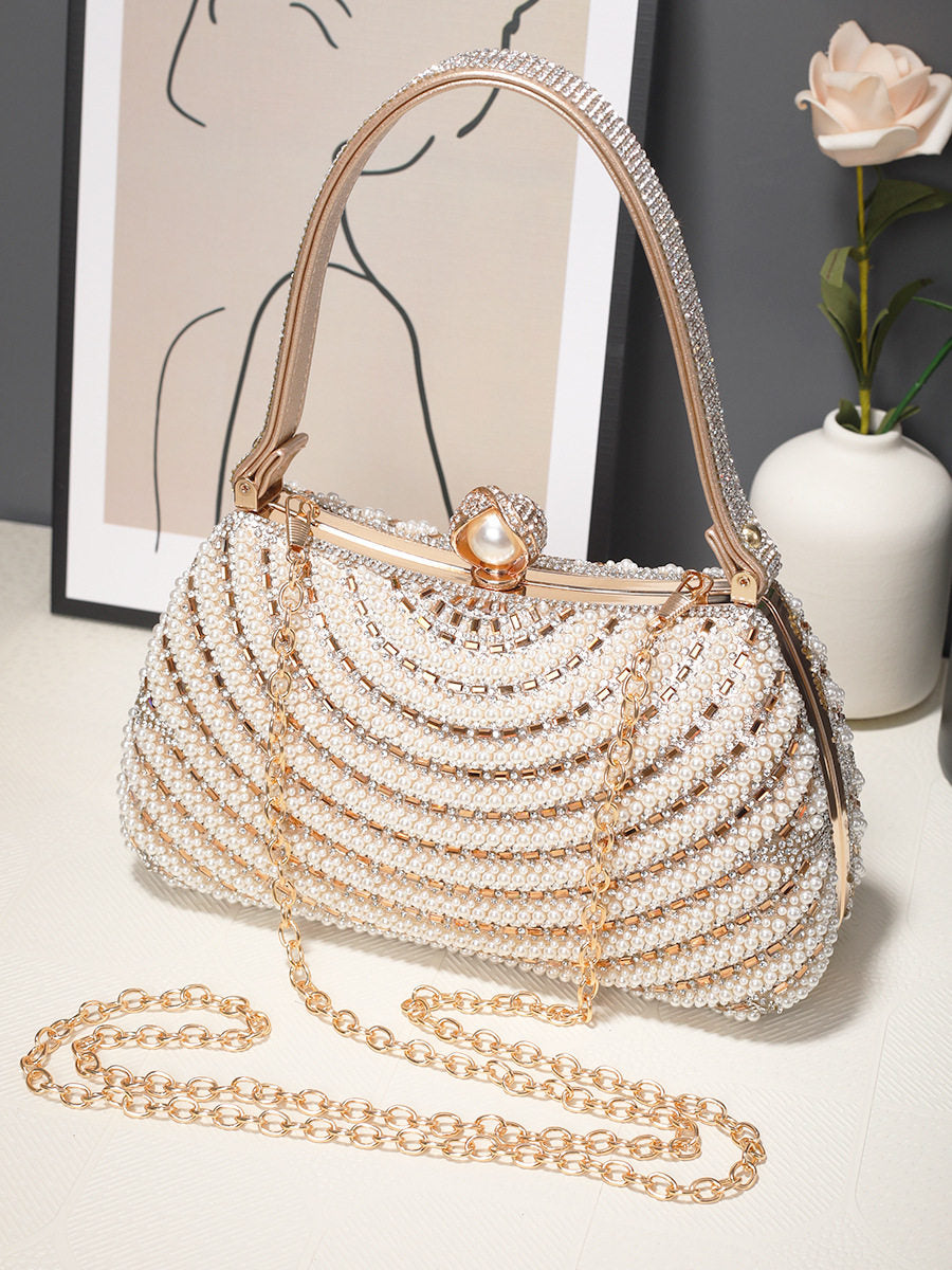 Pearl-handled handbag with chain detail on a light surface with a vase and artwork in the background