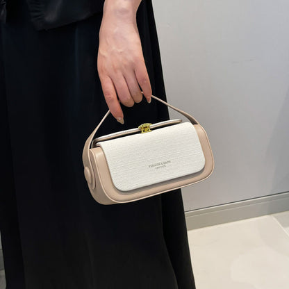 Beige handbag held by a person wearing a black dress against a neutral background