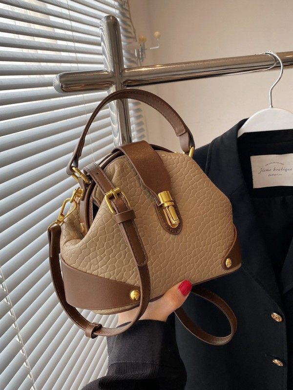 Beige handbag with brown accents held by a person against a blurred indoor background