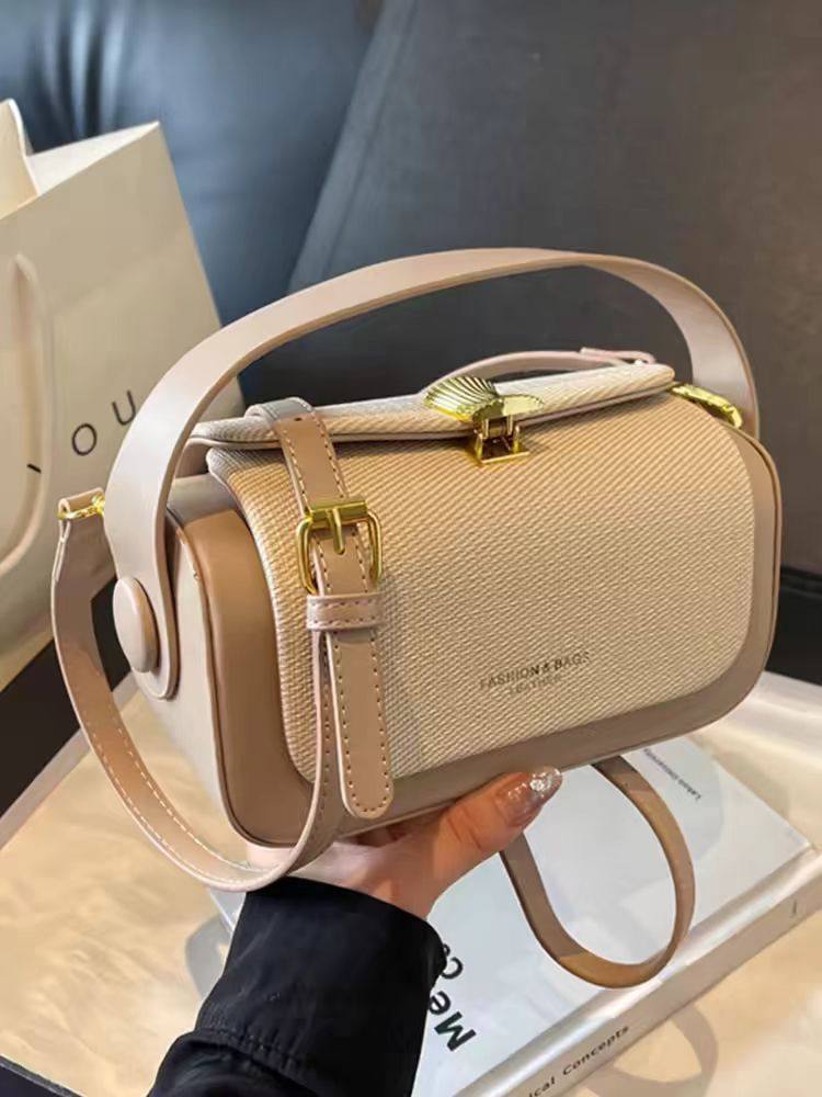 Beige handbag with gold accents held by a person, with a blurred background