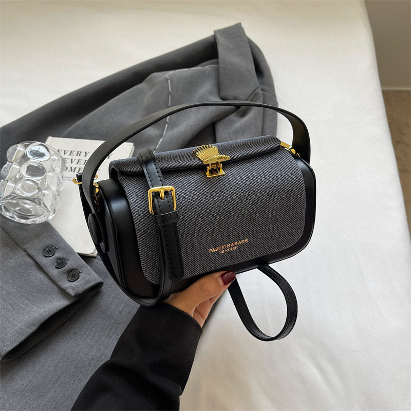 Black handbag with gold accents held by a person, with a gray coat and white surface in the background.