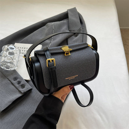 Black handbag with gold accents held by a person, with a gray coat and white surface in the background.