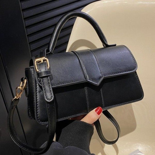 Black handbag with gold buckle held by a person with red nail polish.