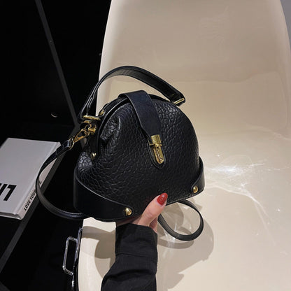 Black textured handbag with gold accents held by a person on a light surface.