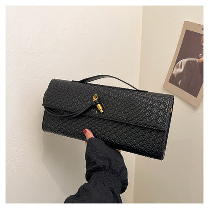 Black woven clutch held by a hand against a neutral background
