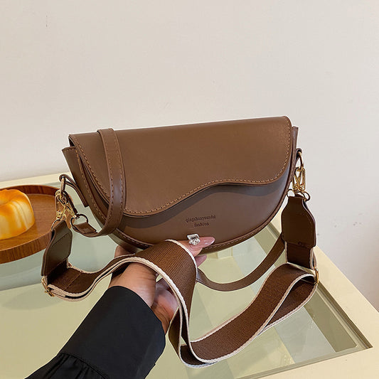 Brown handbag held by a person on a reflective surface with a neutral background