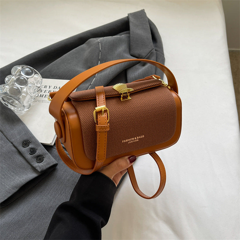 Brown handbag held by a person with a gray coat and glass object in the background