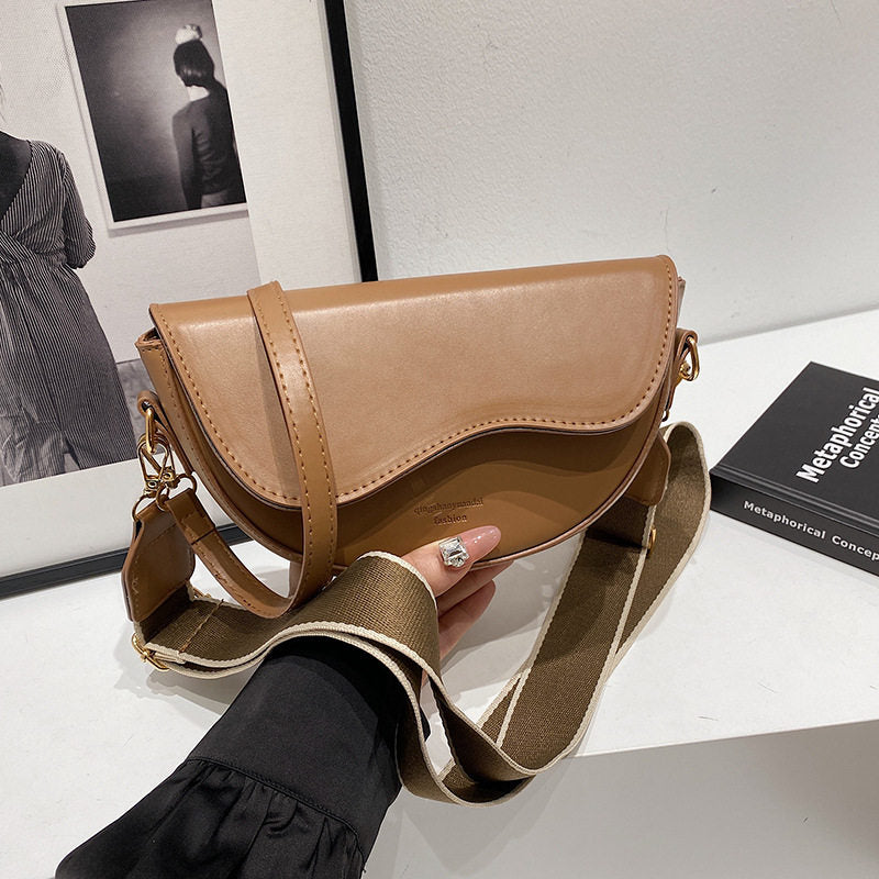 Brown leather handbag held by a person on a reflective surface with a blurred background