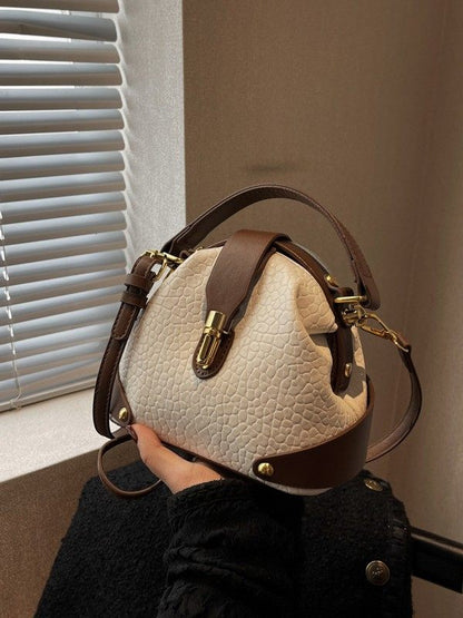 Handbag with brown leather accents held by a person in front of a window.
