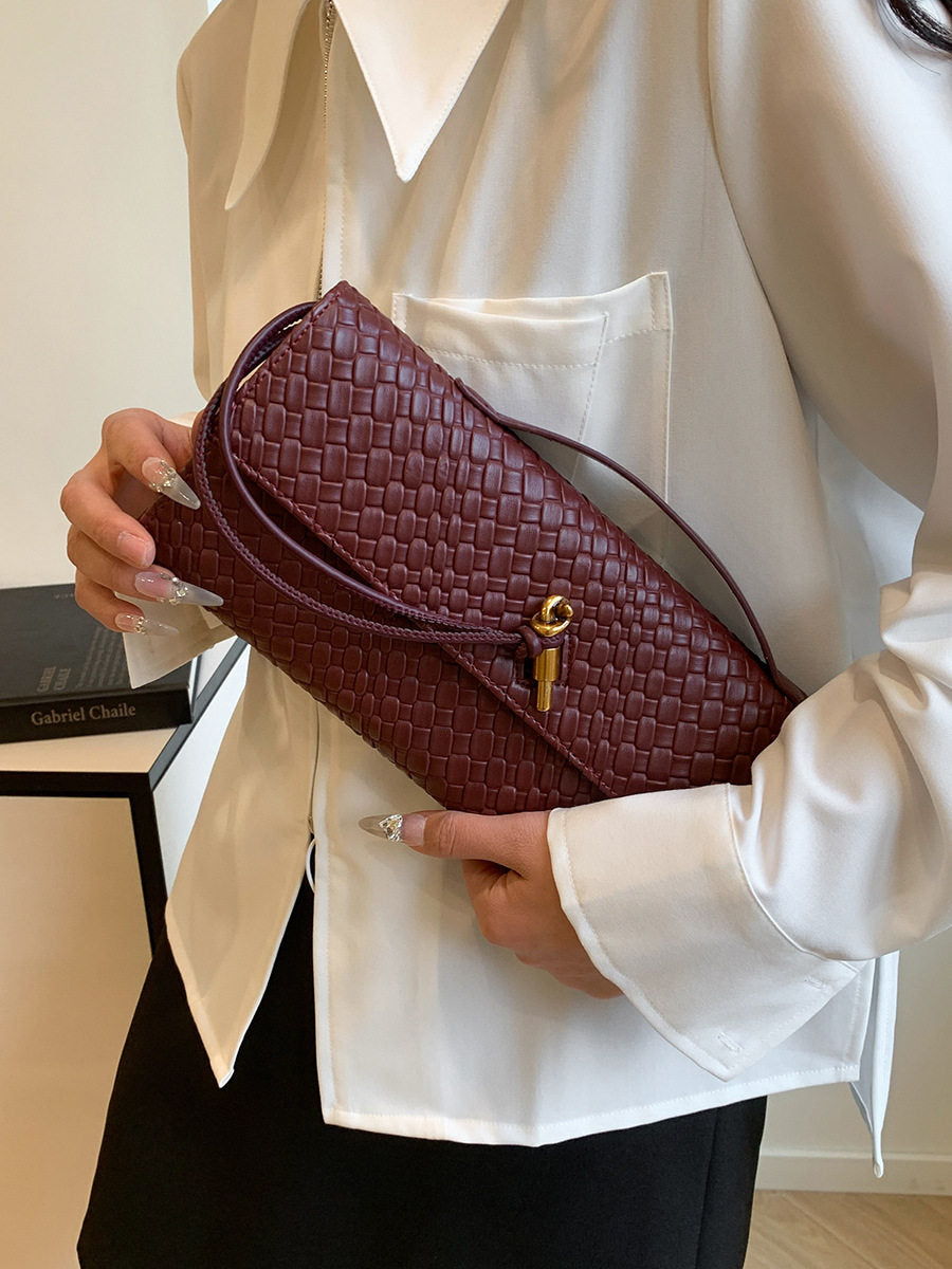 Person holding a maroon woven handbag with a gold clasp.