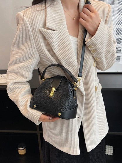 Person wearing a beige ribbed sweater holding a black handbag indoors.