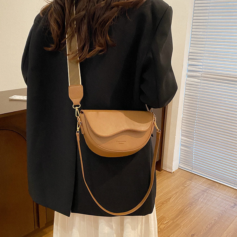Person wearing a black coat with a tan crossbody bag indoors.