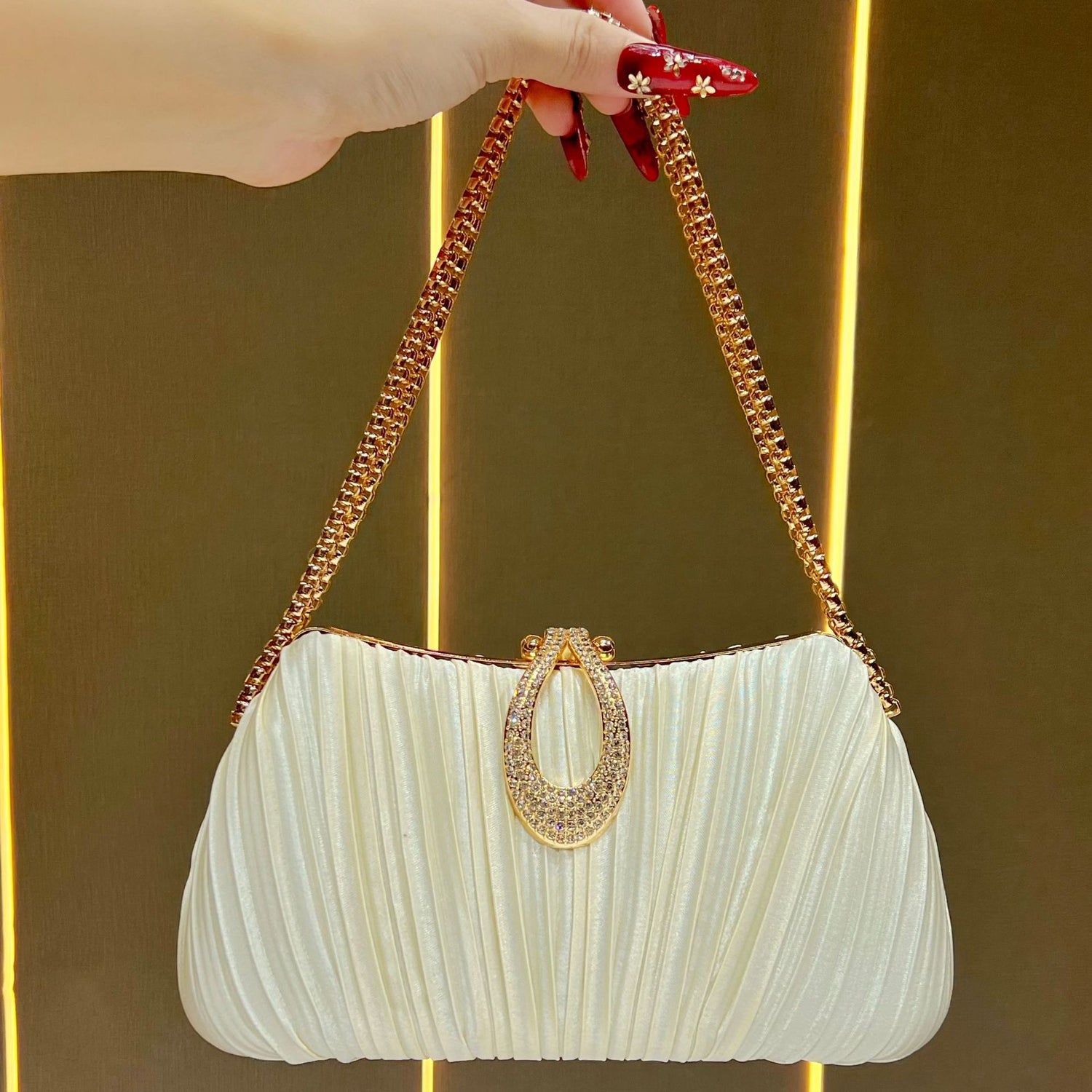 White pleated handbag with gold chain handle held by a hand against a gold background