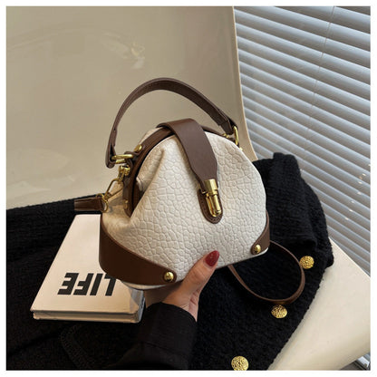 White textured handbag with brown accents held by a hand, placed on a black textured surface with a blurred background.