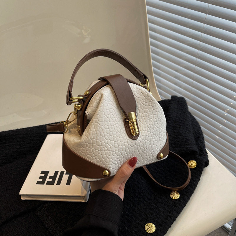 White textured handbag with brown accents held by a person, placed on a black surface with a blurred background.